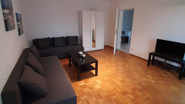 Uma sala de estar com um sofá escuro, uma mesa de centro, um rack para TV e um guarda-roupa.