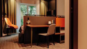 Ein modernes Hotelzimmer mit Schreibtisch, zwei Stühlen, Fernseher und einem Fenster mit Vorhängen.