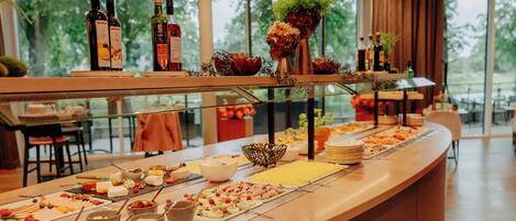 A buffet with various food items and beverages, a glass display case, and a view of the outdoors through large windows.