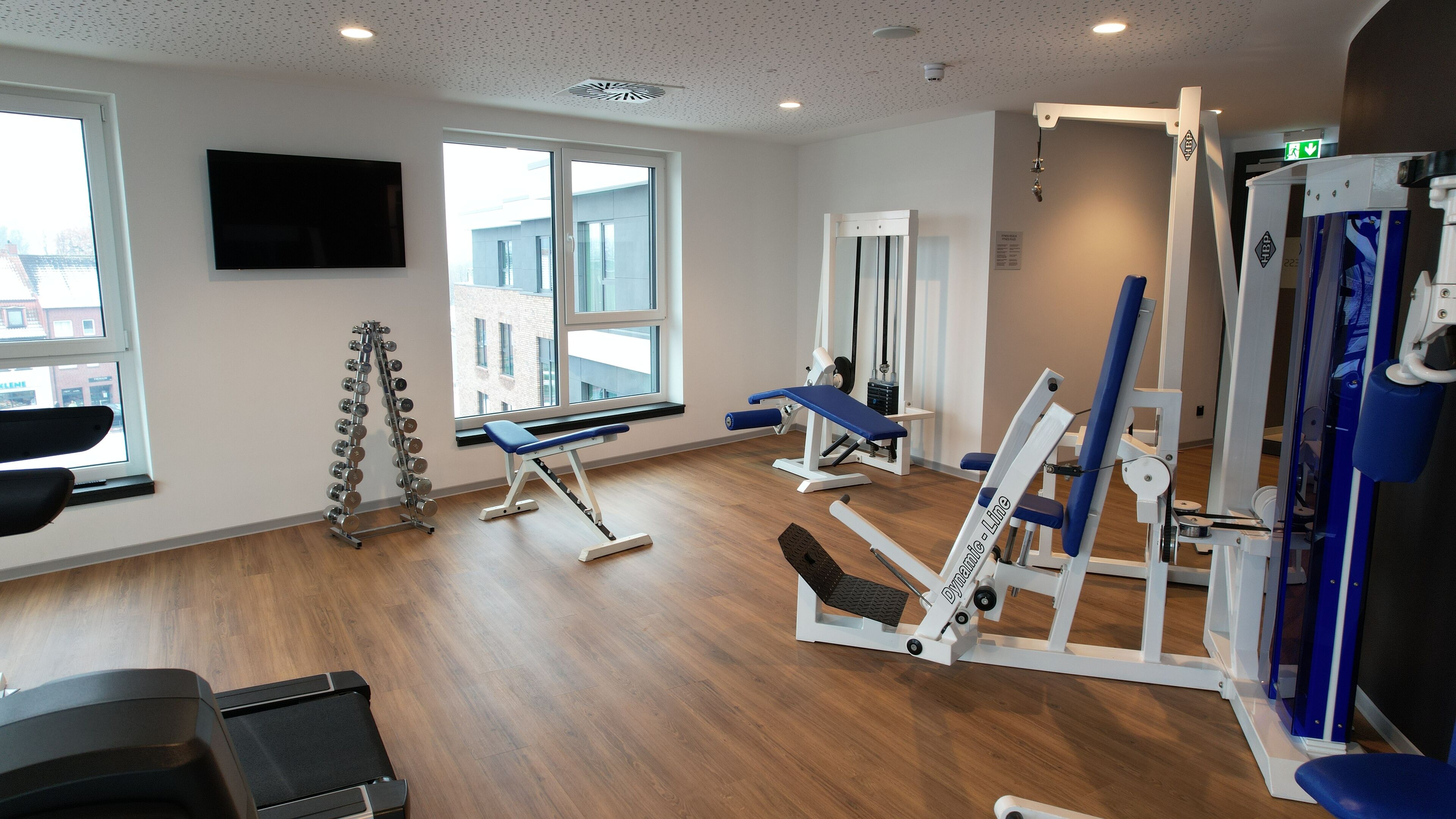 Une salle de sport équipée de matériel d’exercice, d’un téléviseur et de grandes fenêtres.