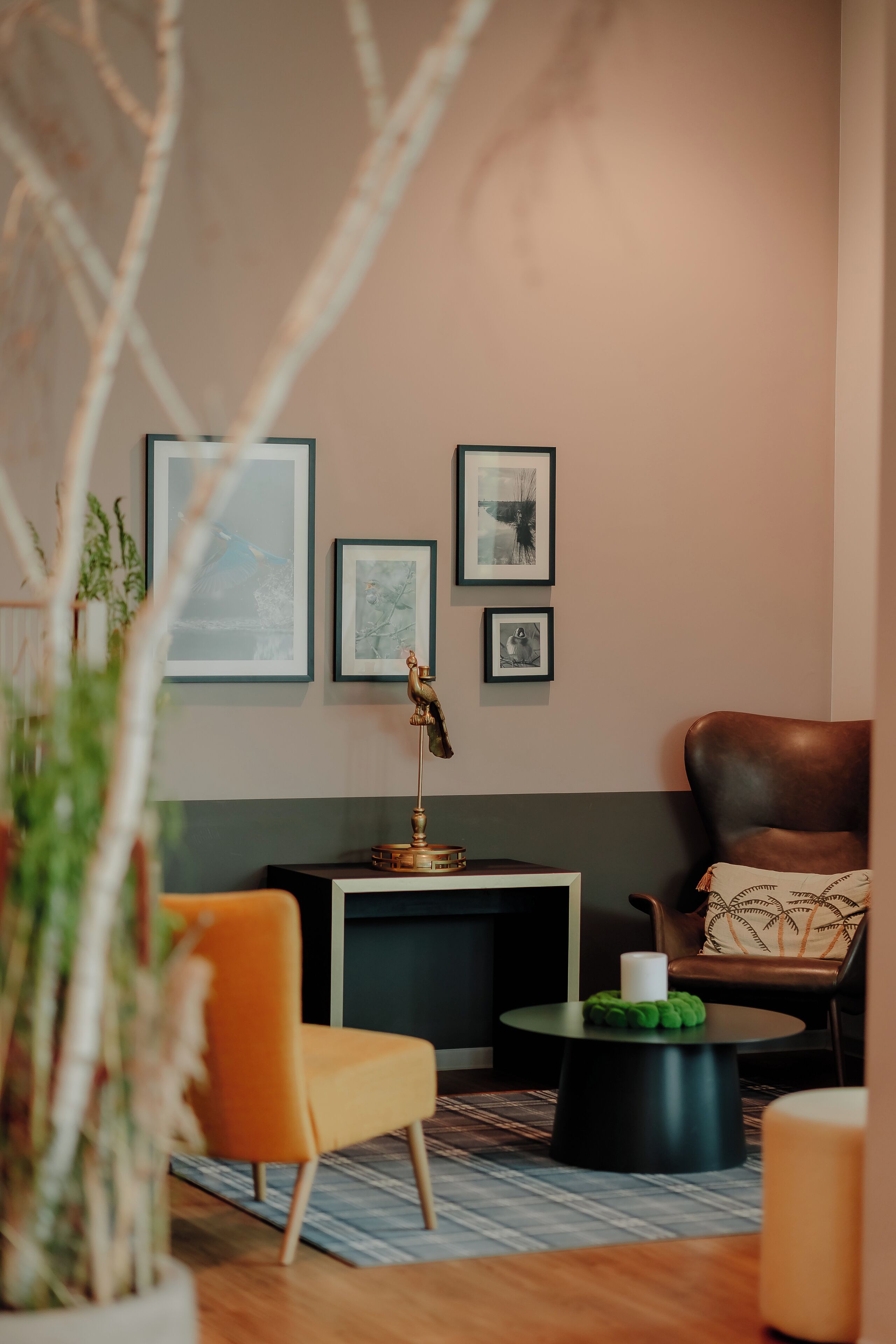 A modern living room with a sofa, a coffee table, and a chair. There are framed pictures on the wall and a lamp on a side table.