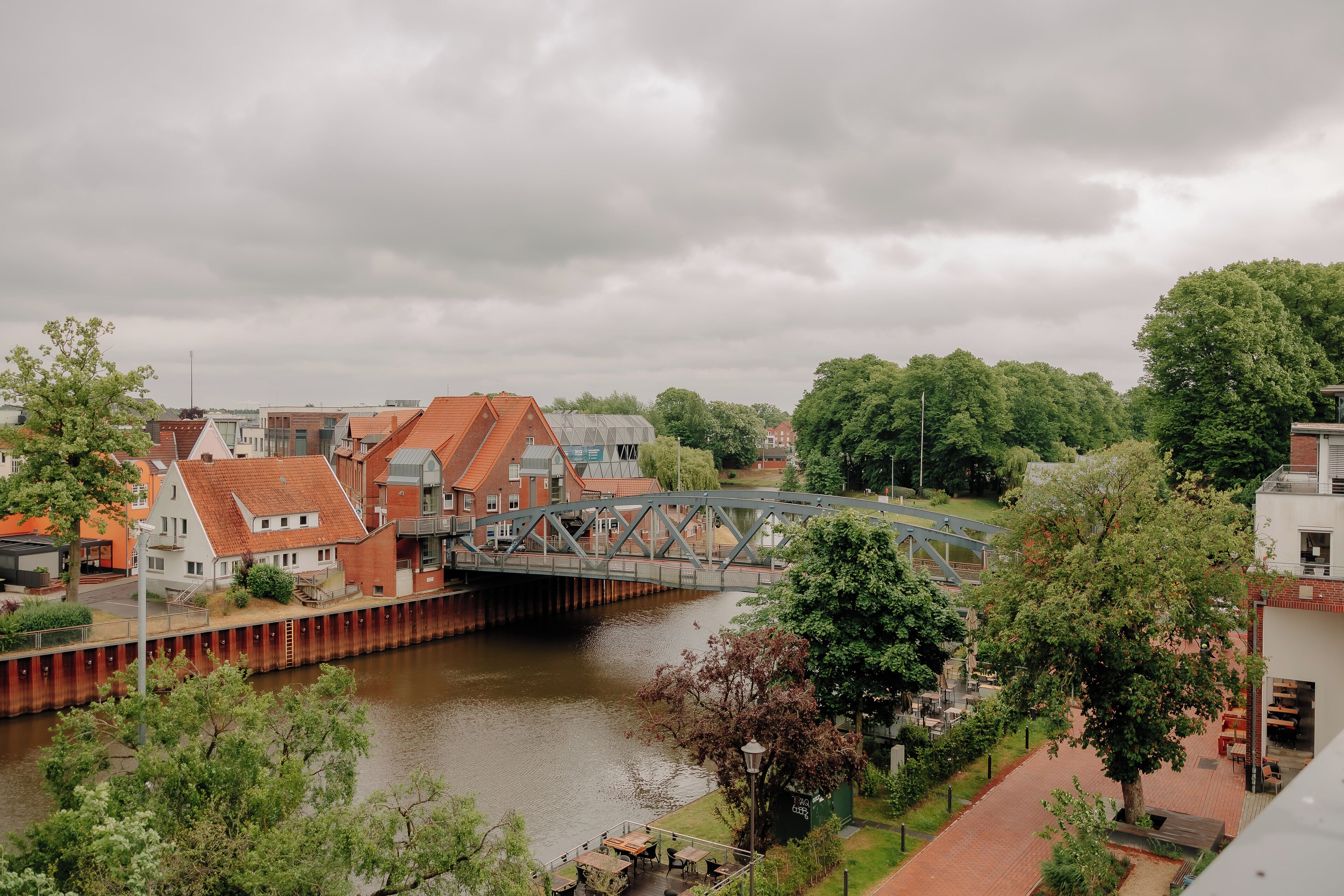 A riverside view with a bridge, buildings, and greenery.