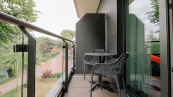 A balcony with a table and chairs, a glass door, and a view of a road and greenery.