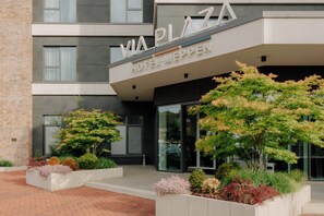 A modern hotel entrance with a name sign, a brick facade, and landscaped gardens. - VIA PLAZA Meppen by Hackmann (Meppen)