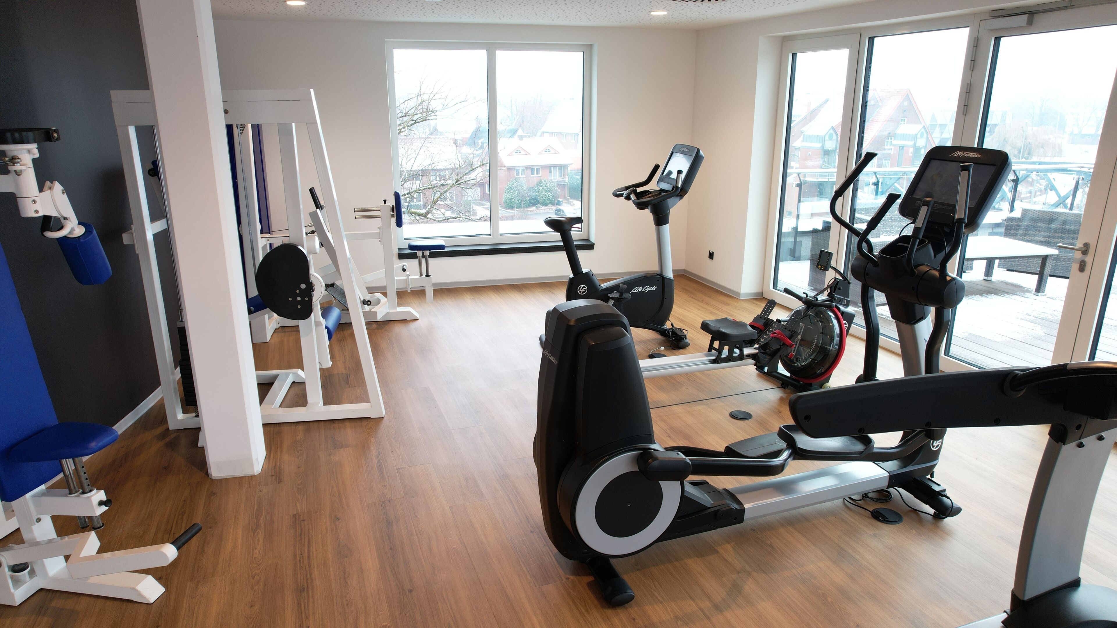 Et fitnesscenter med løbebånd, træningsmaskiner og store vinduer med udsigt ud