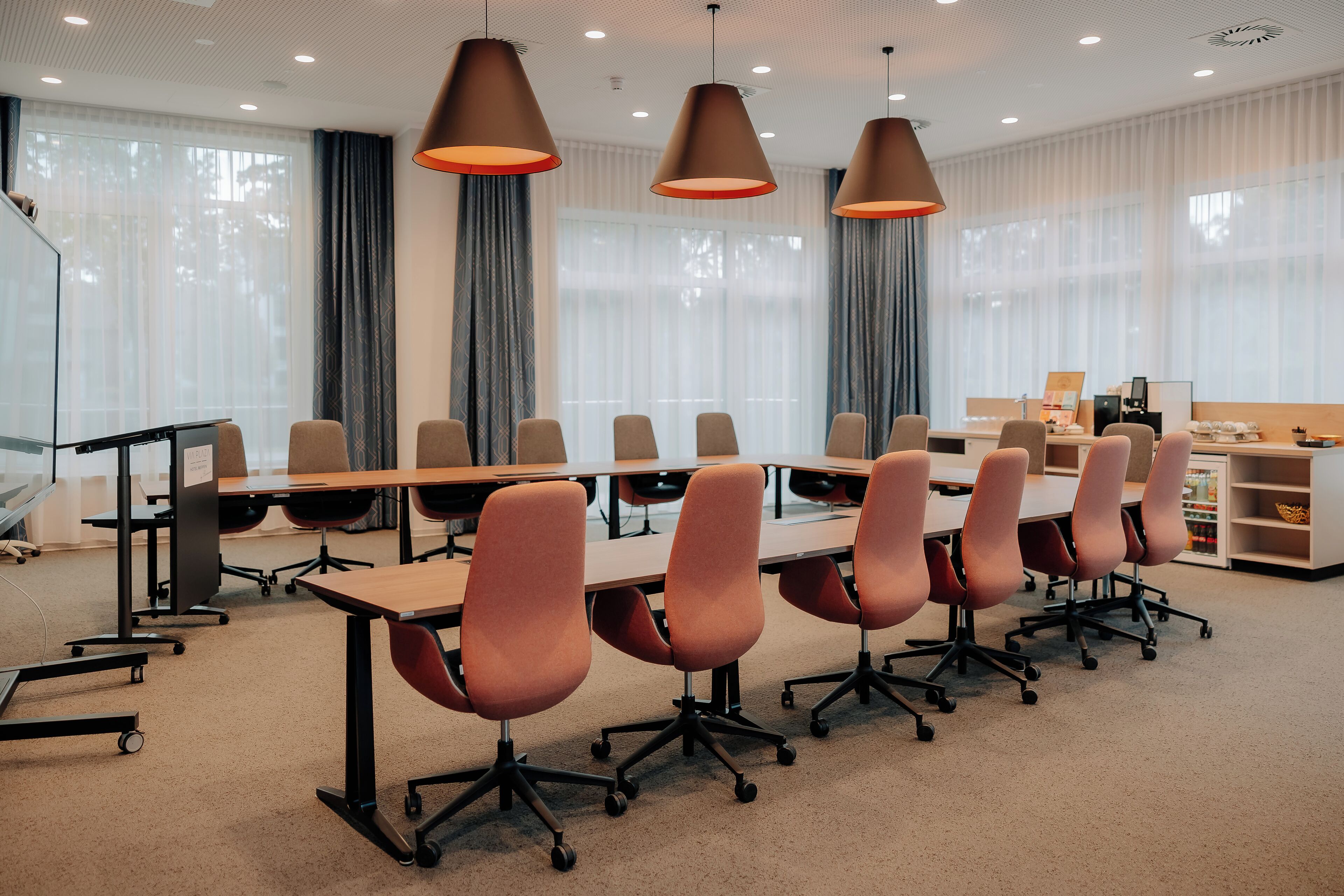 Un salón de conferencias con una larga mesa, varias sillas e iluminación colgante.