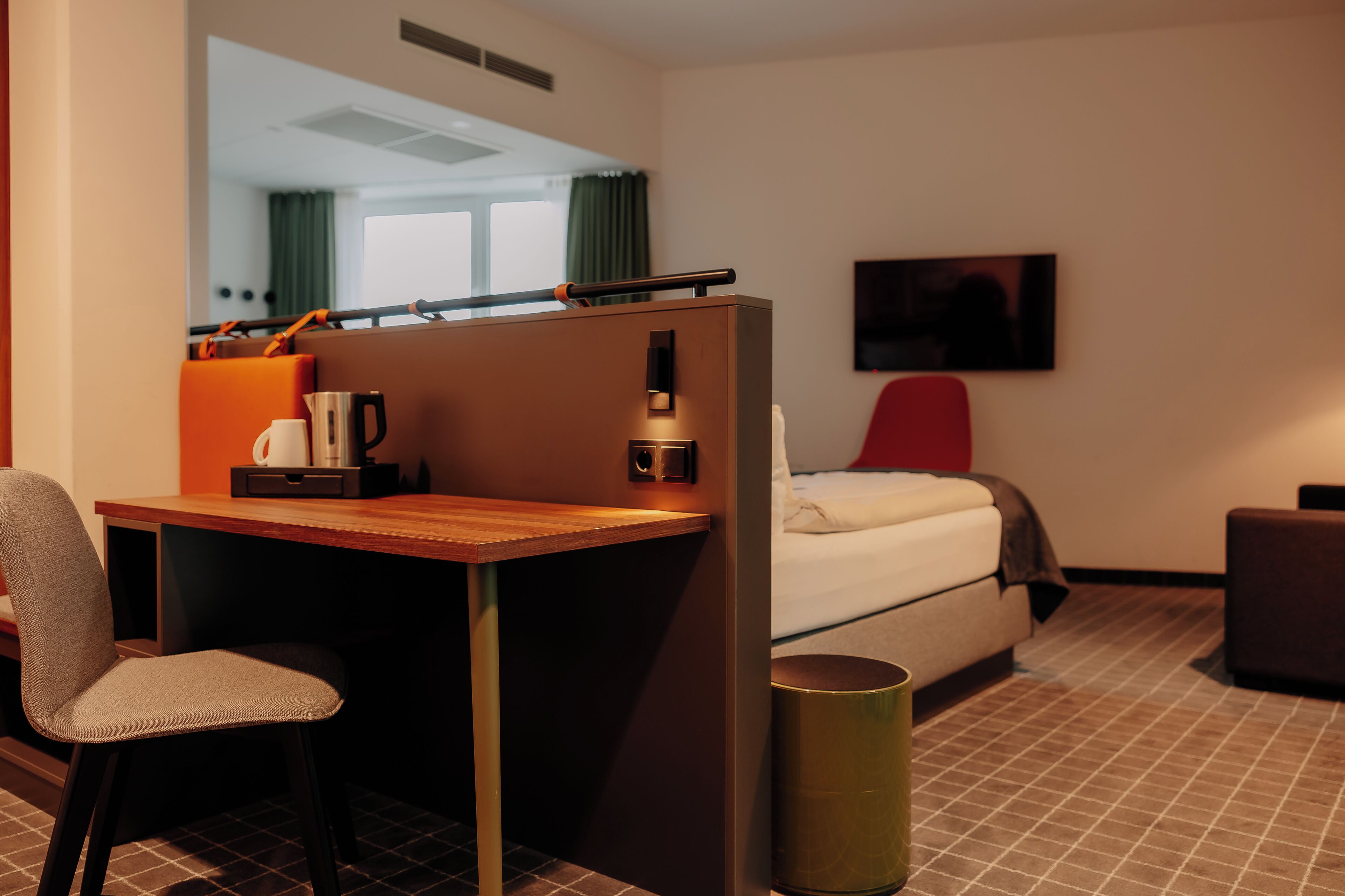 Una habitación de hotel con cama, escritorio, silla, televisor y un cubo de basura.