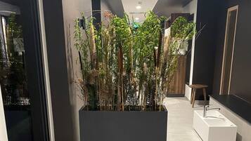 Een moderne hal met een grote plantenbak vol groene planten, een witte badkuip en een houten kruk.