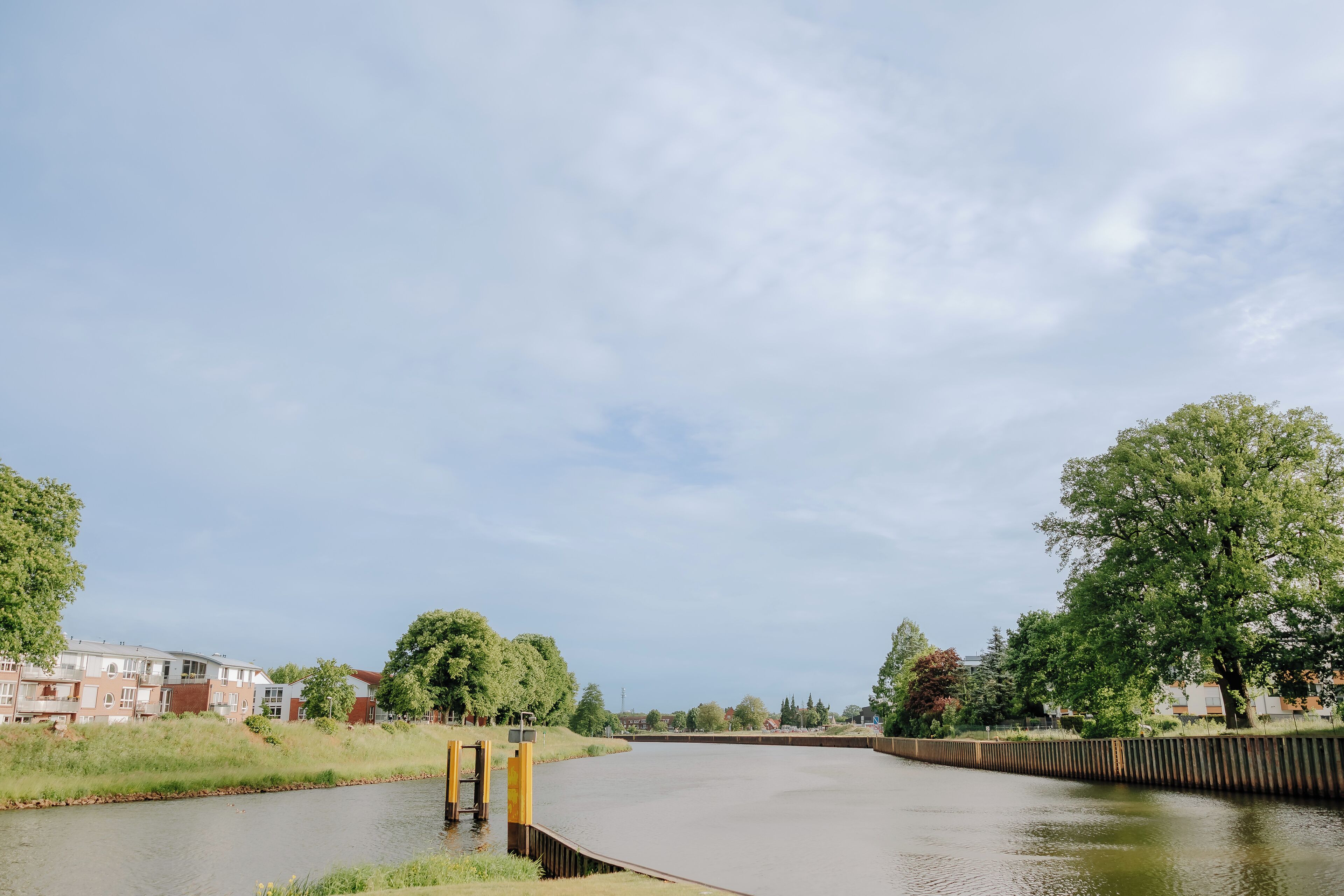 Un paseo junto al río con un sendero curvo, rodeado de vegetación y edificios residenciales.