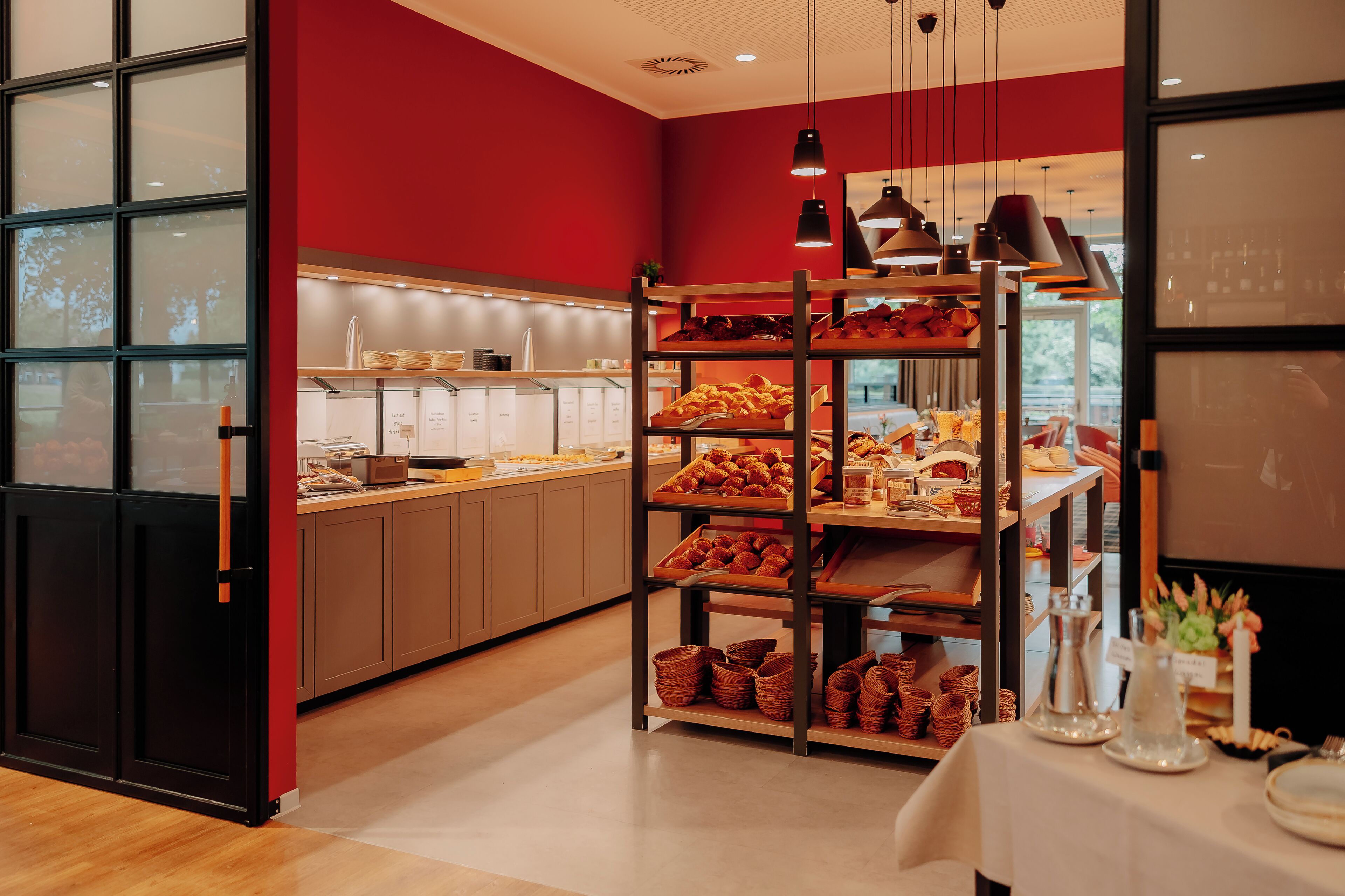 A bakery with shelves of baked goods, a counter with pastries, and a table with serving ware.