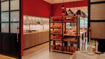 A bakery with shelves of baked goods, a counter with pastries, and a table with serving ware.