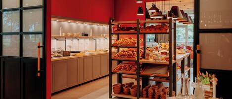 A bakery with shelves of baked goods, a counter with pastries, and a table with serving ware.