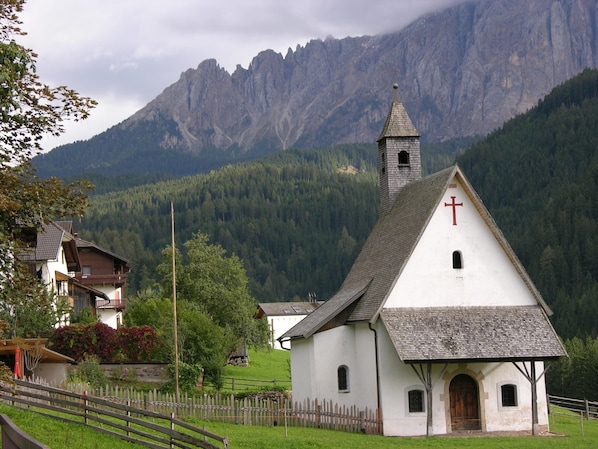 Une petite église blanche, surmontée d’une croix, entourée d’une clôture en bois et avec une chaîne de montagnes en arrière-plan.