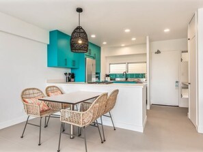 Una cocina moderna con gabinetes color turquesa, una isla central y sillas de mimbre.