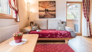 Une pièce confortable avec un canapé-lit, une table en bois agrémentée d’une plante en pot, un tableau au mur et une vue par la fenêtre.
