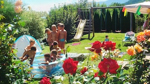 Un jardin avec un toboggan, une balançoire et une petite piscine.
