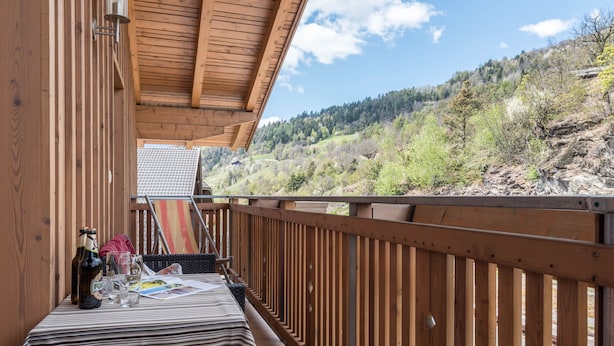 Un balcon en bois avec une table, une bouteille et des verres.