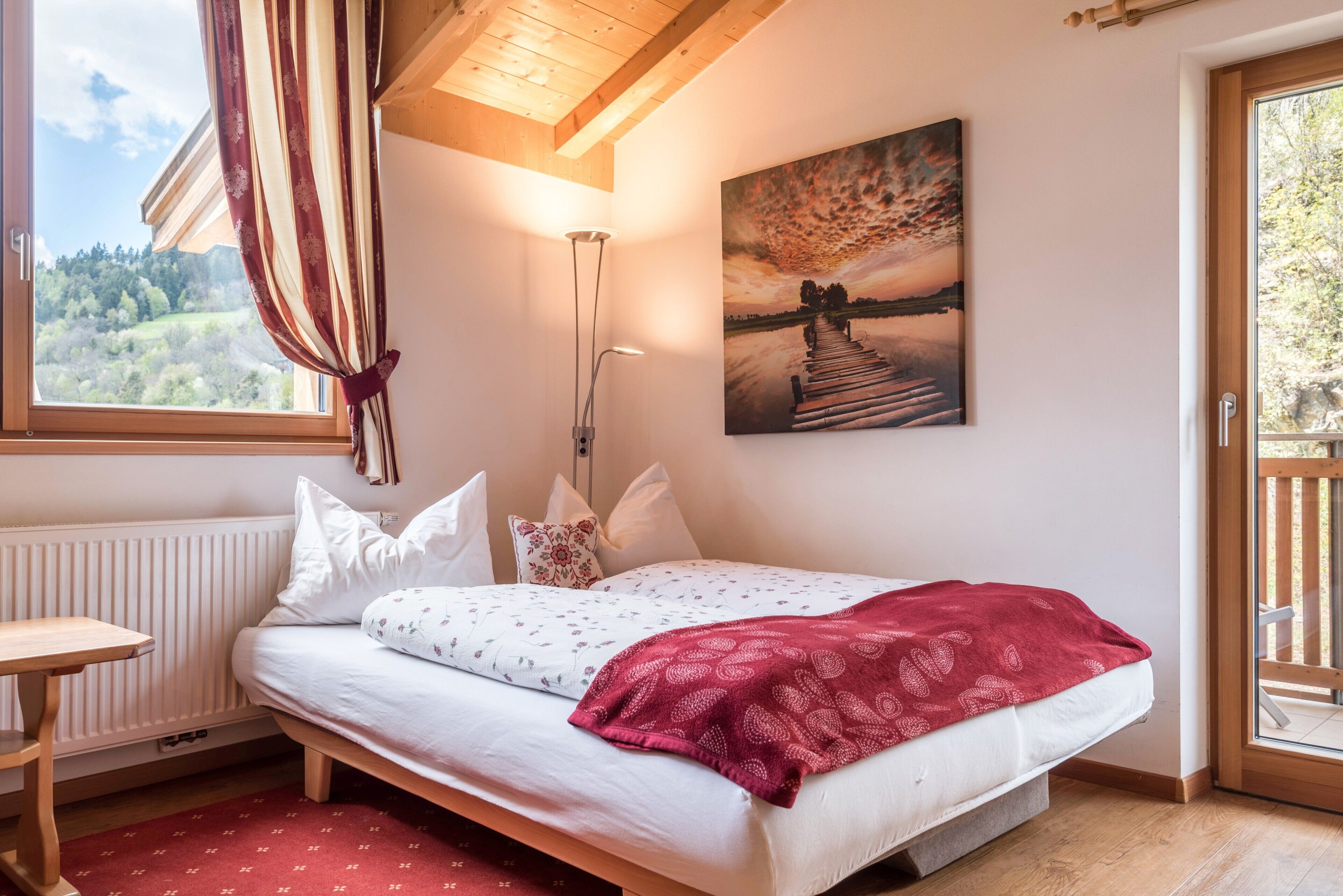 Een slaapkamer met een bed, gordijnen voor het raam, een schilderij, een nachtkastje en een radiator.