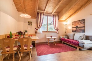 A cozy room with wooden furniture, a dining table, a sofa, and a window with curtains.