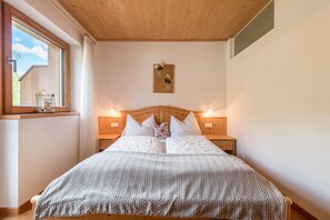 A bedroom with a wooden headboard, a bed with white bedding, two bedside lamps, and a window with a view of a building.