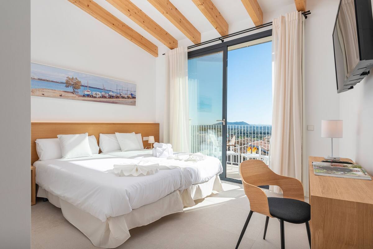 A hotel room with a bed, a desk, a chair, a TV, and a balcony with a view.