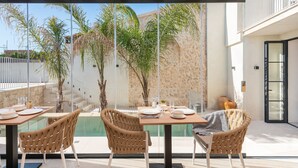 An outdoor dining area with a pool view, wicker chairs, and a stone wall. - Placeta Vella Turismo de Interior (Selva)