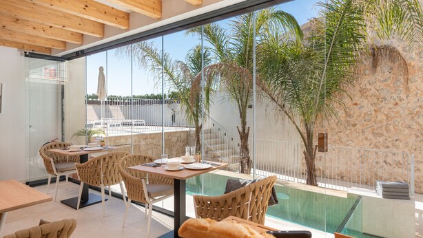 A modern outdoor dining area with wicker chairs and tables, overlooking a swimming pool and palm trees. - Placeta Vella Turismo de Interior (Selva)