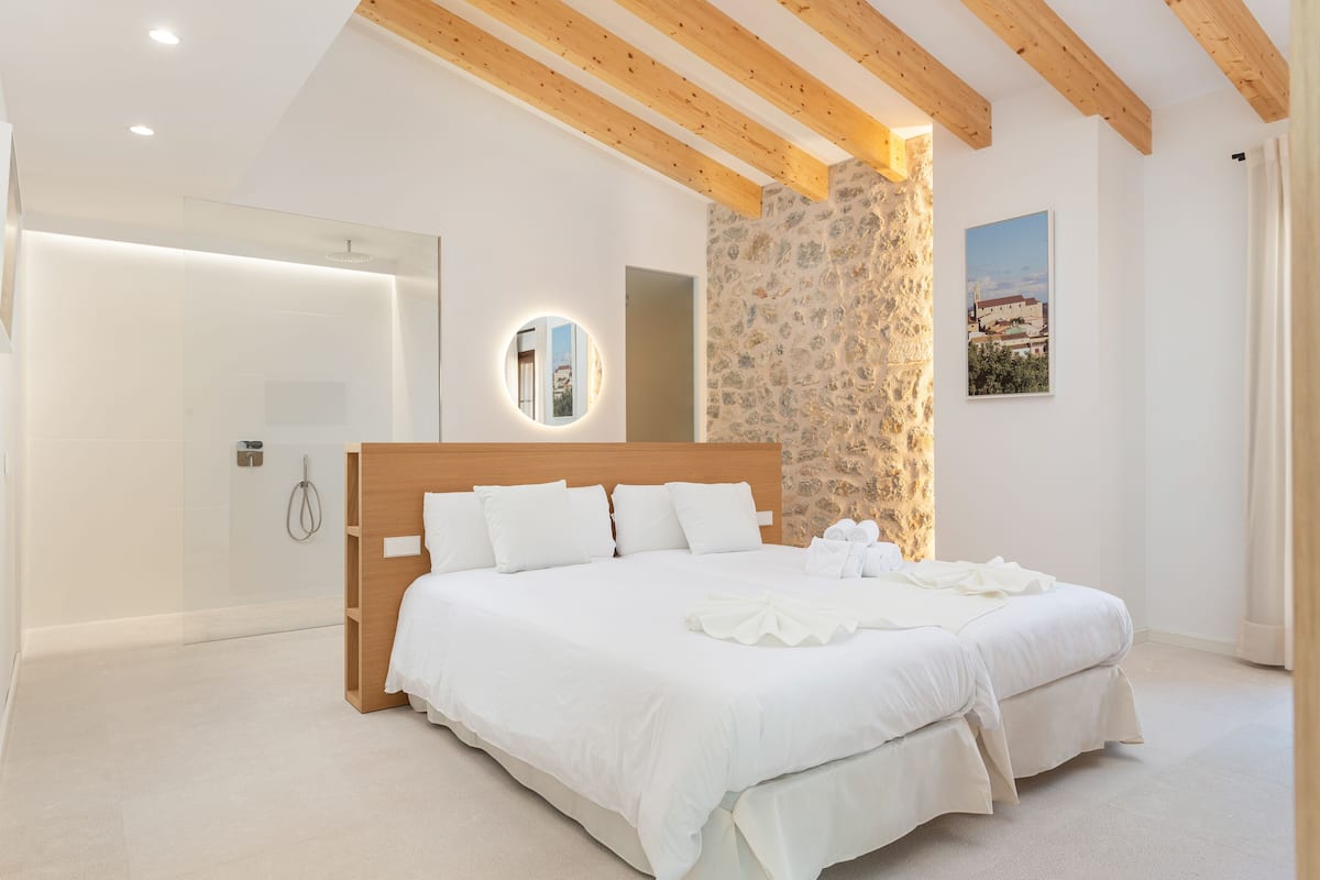 A bedroom with a large bed, wooden beams, a stone wall, and a framed picture on the wall.