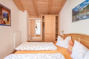 A bedroom with two beds, wooden headboard, a radiator, and a painting of a mountain landscape.