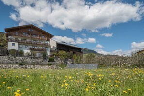 A multi-story building with balconies, a stone retaining wall, and a field of wildflowers.