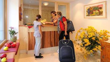 A reception desk with a wooden counter, a vase with flowers, and a painting on the wall.