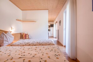 Camera da letto con due letti, soffitto in legno, angolo cottura sullo sfondo e decorazione a forma di cuore al muro.