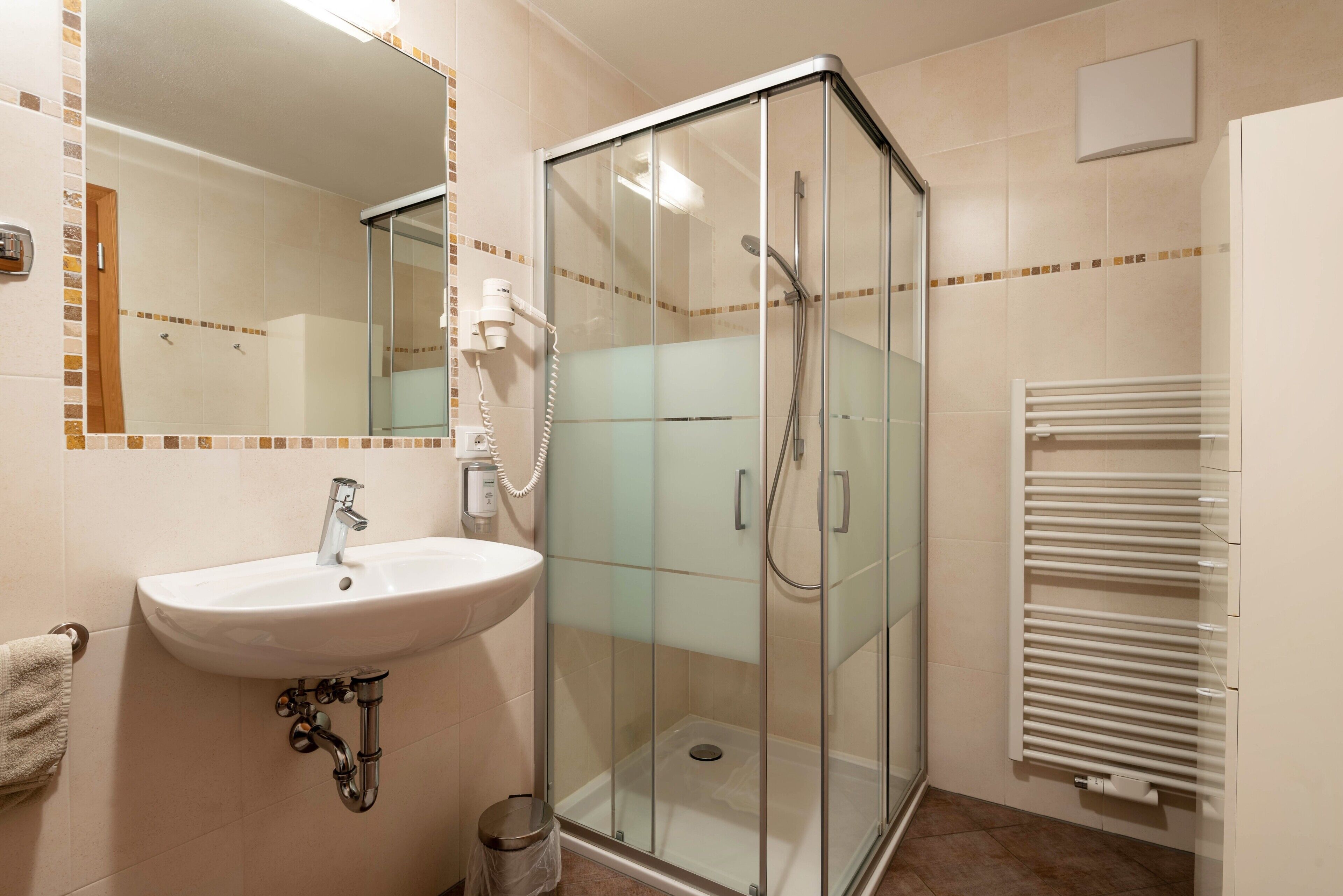 A bathroom with a glass-enclosed shower, a sink, a mirror, and a towel rack.