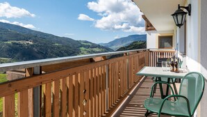 Een balkon met uitzicht op een bergachtig landschap, een tafel met stoelen en een biertje.