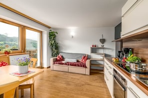 A modern kitchen with a dining area, a sofa, and a large window overlooking a scenic view.