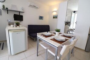 Uma cozinha compacta com geladeira, uma mesa de jantar posta para dois e um sofá ao fundo.