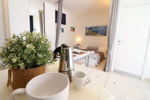 Quarto com cafeteira, caneca branca, planta em vaso e pintura na parede.