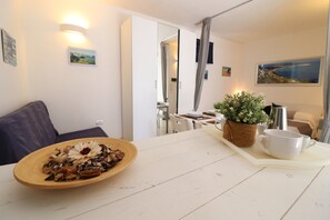 A dining area with a wooden table, a bowl of nuts, a potted plant, and a white mug on a tray.