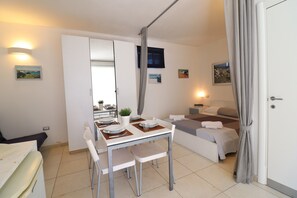 A compact hotel room with a dining area, a bed, a TV, and a bathroom.