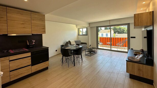 A modern kitchen with wooden cabinets, a dining area with a table and chairs, and a sliding glass door leading to a balcony. - Charming F2 completely renovated in the center of CAVALAIRE SUR MER (CAVALAIRE SUR MER)