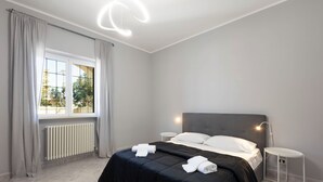 Une chambre d’hôtel moderne avec un grand lit, des tables de chevet, un radiateur et une fenêtre avec des rideaux.