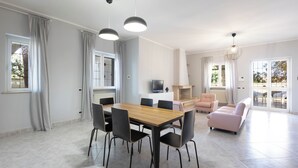 Un vaste espace de vie comprenant une table à manger en bois, des chaises noires, un canapé rose et un téléviseur posé sur un meuble blanc.
