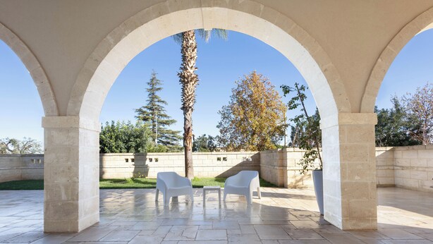 Une terrasse extérieure avec un sol en pierre, deux chaises blanches et un palmier.