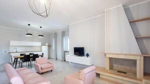 Un salon moderne avec une cheminée, un téléviseur et un coin repas, avec une cuisine en arrière-plan.