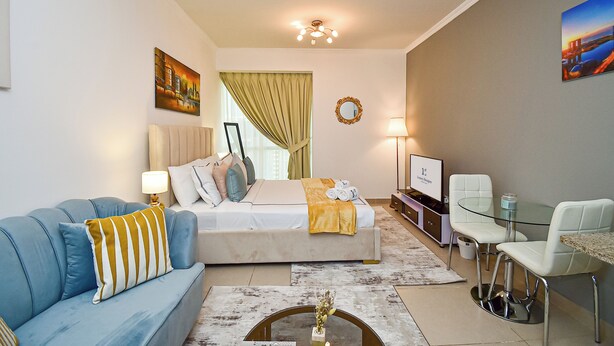 A modern hotel room with a bed, a blue sofa, a glass table, and a TV. - Cozy Studio - Goldcrest Executives JLT - NLN (Dubai)