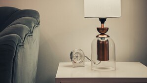 A bedside table with a lamp and an alarm clock. - Cozy Studio - Goldcrest Executives JLT - NLN (Dubai)