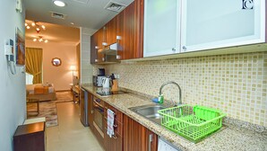 A modern kitchen with wooden cabinets, a granite countertop, a sink, and a green dish rack. - Cozy Studio - Goldcrest Executives JLT - NLN (Dubai)