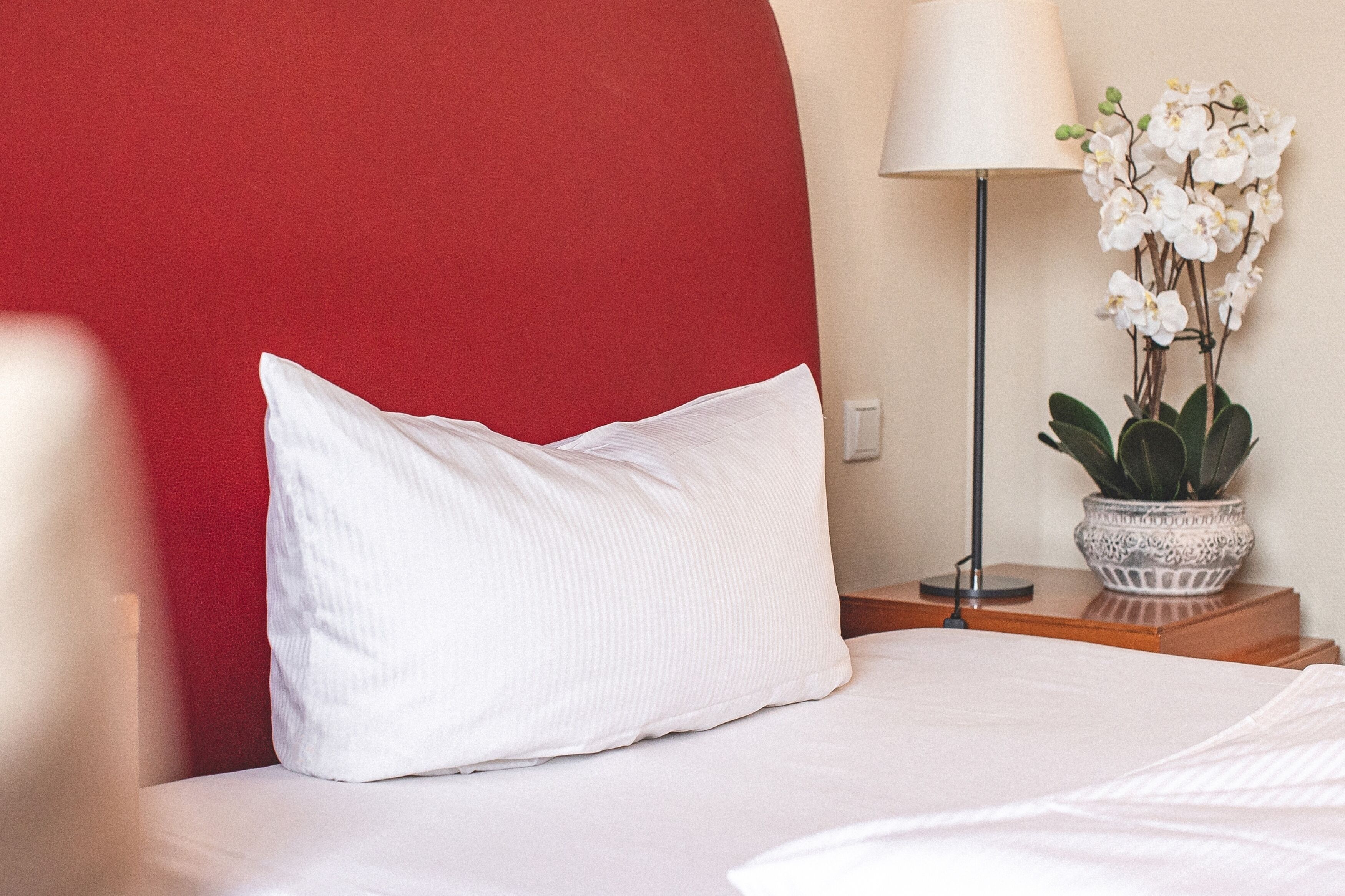 Un lit bien fait, avec un oreiller blanc et une tête de lit rouge.