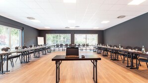 Un salón de conferencias con mesas largas, sillas y un ordenador portátil sobre una de ellas.
