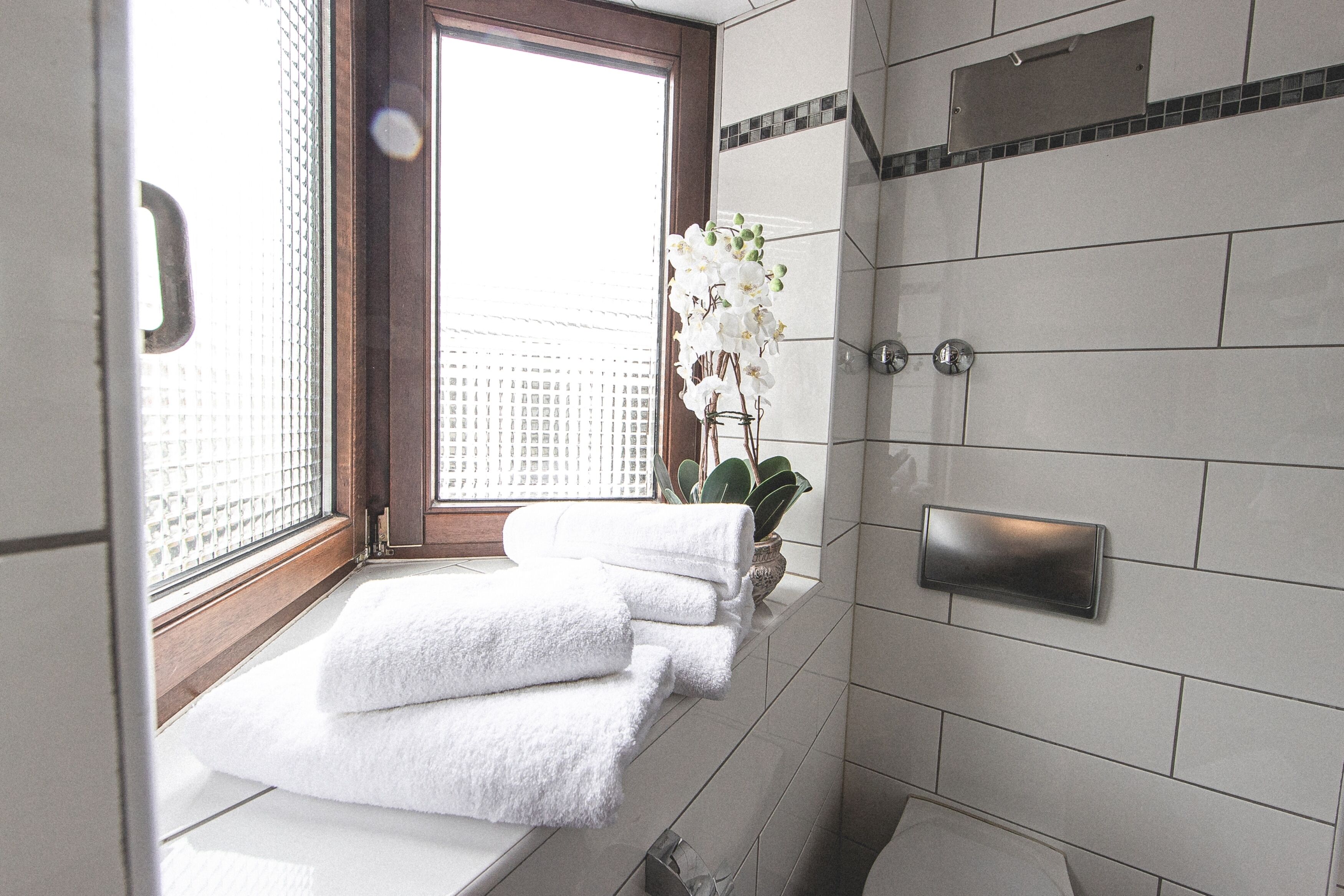 A bathroom with white tiles, a window with blinds, a potted plant, and a towel rack.
